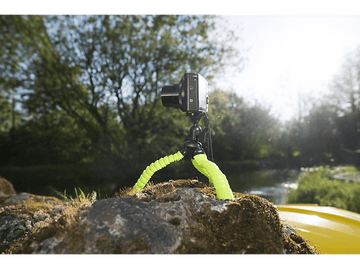 Appareil photo sur un trépied flexible sur un rocher moussue, avec des arbres et un lac en arrière-plan.