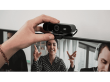 Charger l&#39;image dans la galerie, La main d&#39;une personne ajustant une webcam noire montée sur le dessus d&#39;un écran d&#39;ordinateur.
