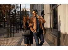 Charger l&#39;image dans la galerie, Couple souriant marchant sur un trottoir. L&#39;homme porte un casque et une veste. Bâtiment en arrière-plan.

