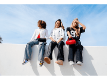 Charger l&#39;image dans la galerie, Trois femmes assises sur un mur blanc, chacune tenant un haut-parleur JBL rouge.
