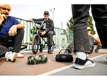 Charger l&#39;image dans la galerie, Groupe de jeunes hommes avec deux enceintes JBL, une camouflée, une noire, sur un terrain de basket-ball, des vélos à proximité.

