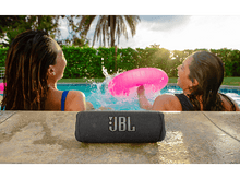Charger l&#39;image dans la galerie, Deux femmes dans une piscine avec une enceinte JBL noire sur le bord. L&#39;une a un gonflable rose.
