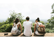 Charger l&#39;image dans la galerie, Trois personnes avec des sacs à dos assises sur un mur de pierre surplombant une vue panoramique.
