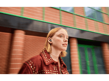 Charger l'image dans la galerie, Une femme aux cheveux blonds porte des écouteurs. Elle porte une veste rouge avec des clous dorés.
