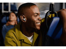 Charger l'image dans la galerie, Homme dans un bus portant des écouteurs, souriant. Intérieur du bus en arrière-plan.
