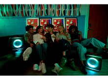 Charger l&#39;image dans la galerie, Cinq jeunes assis sur un canapé avec deux enceintes JBL, éclairés par des lumières colorées et des affiches.
