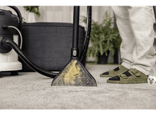 Charger l&#39;image dans la galerie, Un appareil de nettoyage de tapis en cours d&#39;utilisation. La tête de nettoyage est sur le tapis. Une personne est en arrière-plan.
