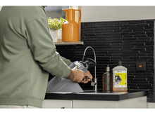 Charger l&#39;image dans la galerie, Homme nettoyant un filtre d&#39;aspirateur dans un évier avec des produits de nettoyage.
