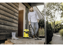 Charger l&#39;image dans la galerie, Homme utilisant un aspirateur jaune sur un porche. Bottes et plantes visibles.
