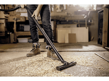Charger l&#39;image dans la galerie, Personne utilisant un aspirateur dans un atelier. Copeaux de bois sur le sol. Fond sombre.
