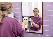 Charger l&#39;image dans la galerie, Femme nettoyant un miroir avec un nettoyeur de vitres blanc et noir dans une salle de bain.
