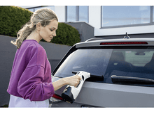 Charger l&#39;image dans la galerie, Femme nettoyant une vitre de voiture avec un nettoyeur de vitres blanc et noir à l&#39;extérieur.
