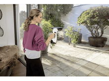 Charger l&#39;image dans la galerie, Femme nettoie fenêtre, arrière-plan arbres, patio, soleil.
