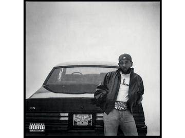 Kendrick Lamar, appuyé sur une voiture noire. Photo en noir et blanc. Il porte une casquette, une veste et une banane.