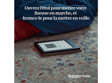 Charger l&#39;image dans la galerie, Une liseuse sur un tapis. L&#39;écran est allumé. Le texte dit: Ouvrir pour démarrer, fermer pour dormir.
