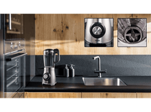 Charger l&#39;image dans la galerie, Scène de cuisine avec mixeur, évier et meubles en bois. Mixeur base argentée.
