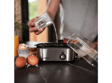 Charger l&#39;image dans la galerie, Une personne verse de l&#39;eau dans un cuiseur à œufs. Œufs et toasts sur le comptoir.
