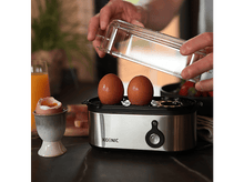 Charger l&#39;image dans la galerie, Des œufs placés dans un cuiseur à œufs, avec un œuf dans un support et du jus d&#39;orange.
