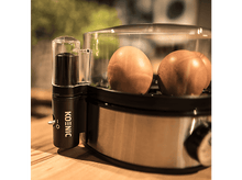 Charger l&#39;image dans la galerie, Un cuiseur d&#39;œufs avec deux œufs à l&#39;intérieur, sur une table en bois.
