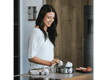 Charger l&#39;image dans la galerie, Femme souriante, plaçant des œufs dans un cuiseur à œufs.
