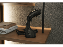 Charger l&#39;image dans la galerie, Un défroisseur de vêtements noir sur une étagère en bois avec des vêtements pliés et une prise de courant.
