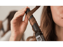 Charger l&#39;image dans la galerie, Une personne se boucle les cheveux avec un fer à friser. Les cheveux sont enroulés autour du fer.
