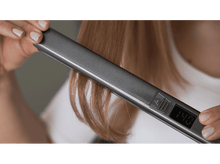 Charger l&#39;image dans la galerie, Une personne utilisant un lisseur sur des cheveux blonds, l&#39;appareil affiche la température.
