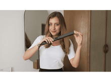 Charger l&#39;image dans la galerie, Femme utilisant un lisseur. Elle se regarde dans le miroir. Chemise blanche.
