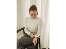 Charger l&#39;image dans la galerie, Femme assise, mesurant sa tension artérielle avec un moniteur numérique de poignet. Elle regarde l&#39;appareil.

