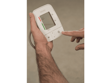 Charger l&#39;image dans la galerie, Une main appuie sur le bouton d&#39;alimentation d&#39;un tensiomètre blanc. Gros plan.
