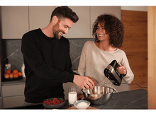 Charger l&#39;image dans la galerie, Couple dans la cuisine mélangeant des ingrédients. L&#39;homme ajoute un œuf au bol. Framboises, lait, sucre.
