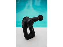 Charger l&#39;image dans la galerie, Pistolet de massage noir avec tête ronde, sur une surface blanche, piscine en arrière-plan.
