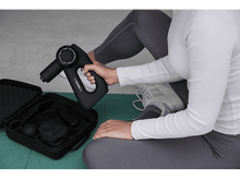 Charger l&#39;image dans la galerie, Une personne tient un pistolet de massage noir, avec l&#39;étui ouvert et accessoires visibles.
