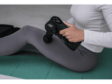 Charger l&#39;image dans la galerie, Femme utilisant un pistolet de massage Koznic sur sa jambe, sur un tapis de yoga vert.
