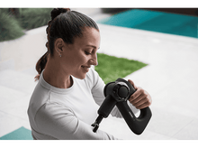 Charger l&#39;image dans la galerie, Femme utilisant un pistolet de massage noir sur son bras à l&#39;extérieur près d&#39;une piscine.
