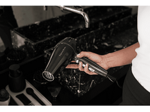 Charger l&#39;image dans la galerie, Femme tenant un sèche-cheveux noir dans une salle de bain, gros plan.
