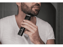 Charger l&#39;image dans la galerie, Homme taillant sa barbe avec une tondeuse noire. Chemise blanche, barbe de trois jours.

