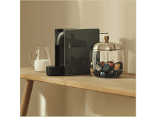 Charger l&#39;image dans la galerie, Machine à café, pichet à lait, récipient en verre avec capsules. Surface en bois. Couleurs neutres.
