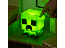 Charger l&#39;image dans la galerie, Lampe Creeper verte Minecraft sur une table de nuit. Une main touche la lampe. Il y a un livre à proximité.
