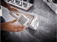 Charger l&#39;image dans la galerie, Des mains tiennent une machine à glaçons blanche avec une grille pour séparer les cubes. Plan de travail de cuisine en arrière-plan.
