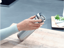 Charger l&#39;image dans la galerie, La main d&#39;une personne tenant une bouteille isotherme argentée et noire. Le fond montre une cuisine.
