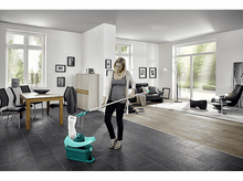 Charger l&#39;image dans la galerie, Une femme lave un sol carrelé sombre. Un seau de nettoyage est au premier plan.
