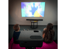 Charger l&#39;image dans la galerie, Projecteur affichant un dessin animé. Deux enfants sont assis sur un tapis rose, regardant.
