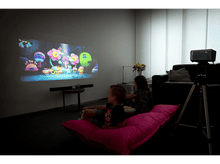 Charger l&#39;image dans la galerie, Deux enfants regardant un film projeté sur un mur. Il y a un projecteur et une barre de son dans la pièce.
