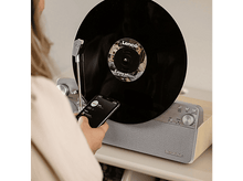 Charger l&#39;image dans la galerie, Une femme utilise un téléphone près d&#39;une platine avec un disque vinyle.
