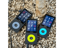 Charger l&#39;image dans la galerie, Trois lecteurs MP3 Lenco noirs sur une surface de petits cailloux. Chacun a un écran et un bouton de couleur différente.
