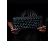 Charger l&#39;image dans la galerie, Clavier noir tenu par des mains. Touches rétro-éclairées bleues, touches noires, logo Logitech.
