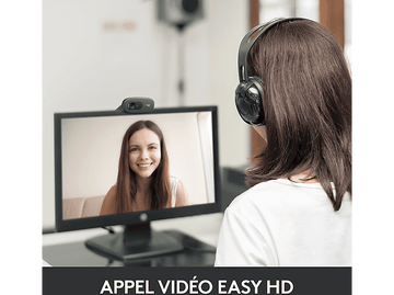 Femme portant un casque regardant un écran d'ordinateur avec une webcam.