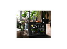 Charger l&#39;image dans la galerie, Une station météo noire affichant des données météo, avec une icône de soleil, sur une table en bois.
