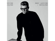 Image en noir et blanc de Marc Lavoine en manteau noir et lunettes, appuyé sur une surface.